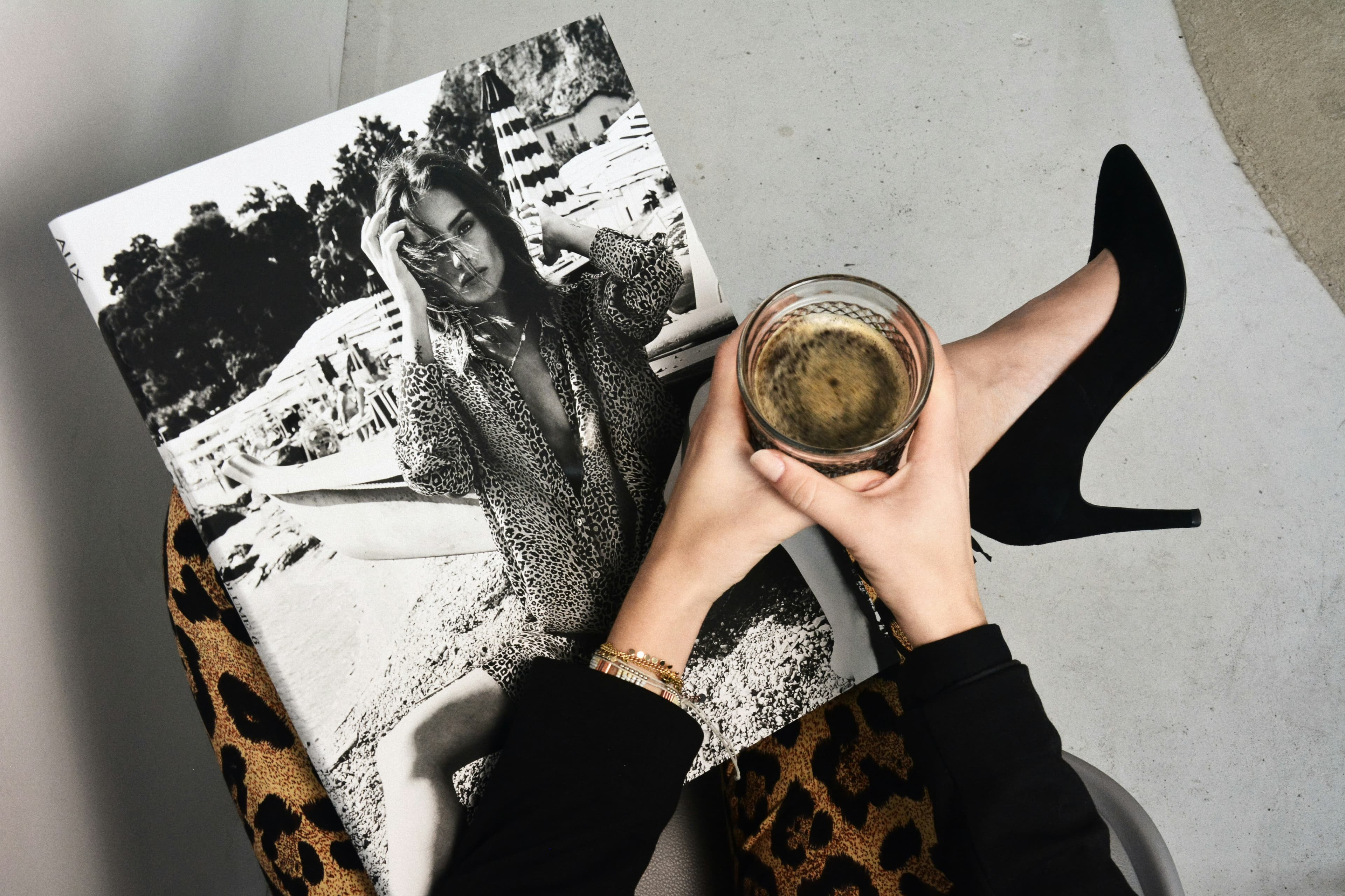 Hands holding a glass over a photo book, black pump and leopard print